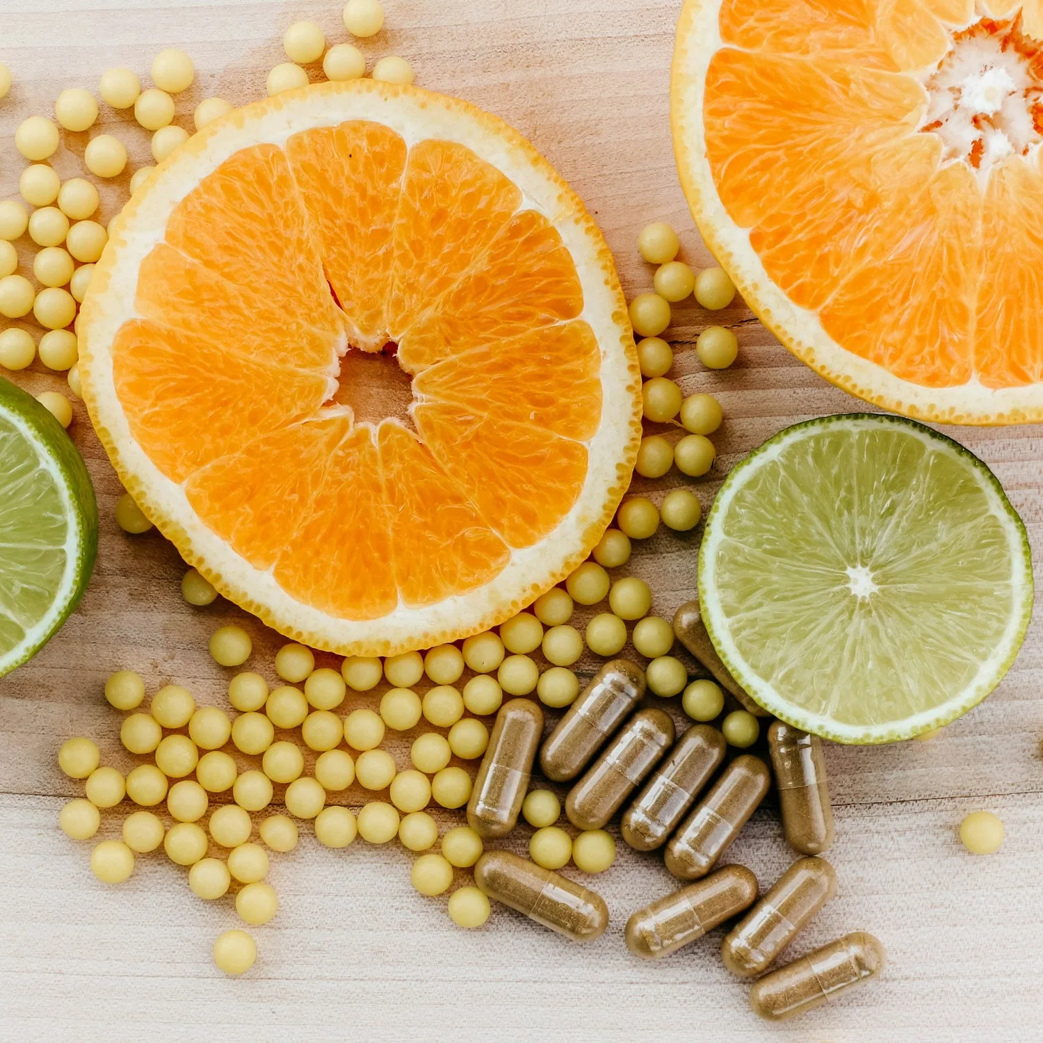 Kapsle doplňků stravy a vitamínové kuličky vedle plátků pomeranče a limetky
