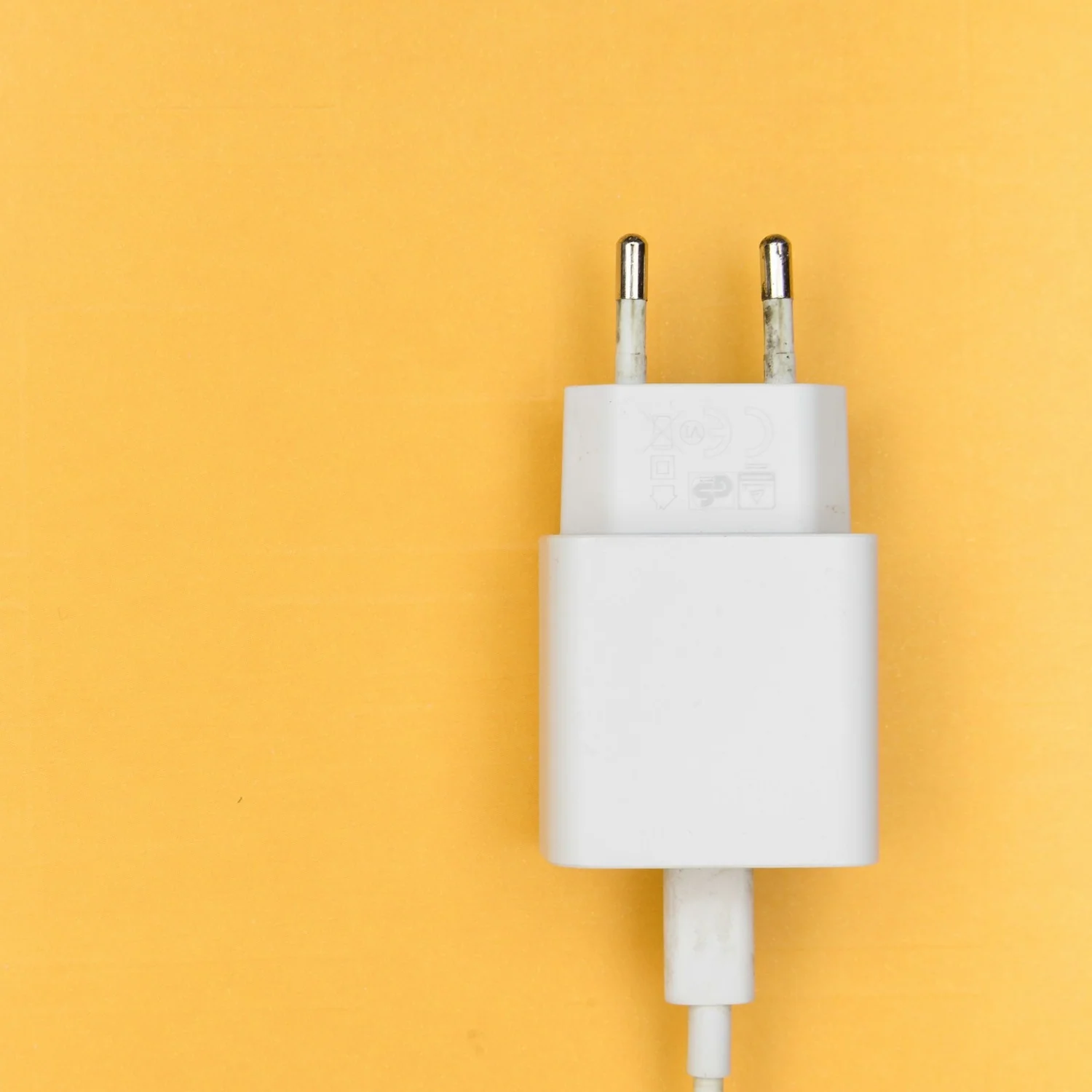 Bílá USB nabíječka s evropskou zástrčkou a kabelem na žlutém pozadí